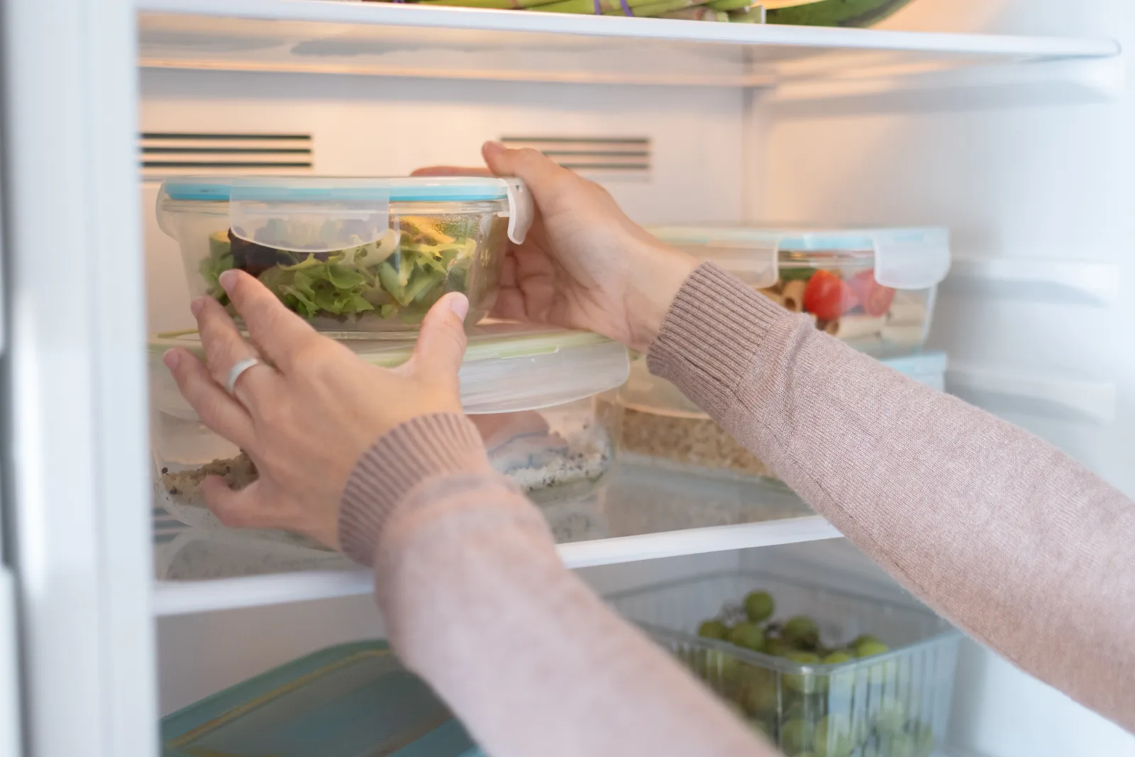 A woman stores a glass meal-prep container in the refrigerator.