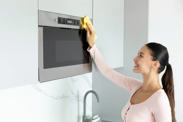 A woman uses a soft yellow cloth to clean microwave grease safely.